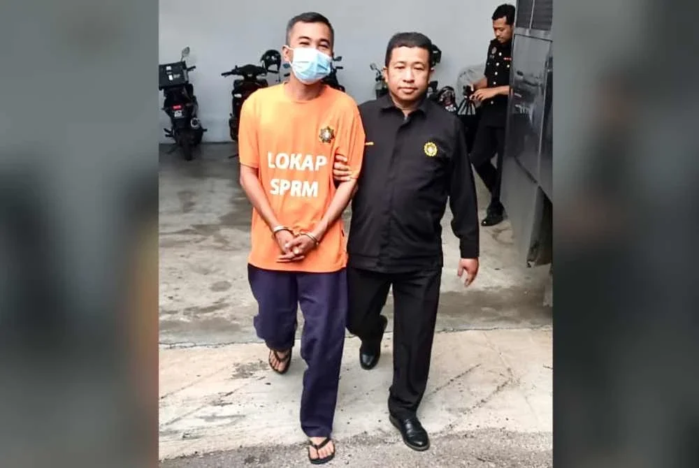 Suspek (kiri) dikawal anggota SPRM ketika keluar dari lokap mahkamah selepas selesai mengambil perintah reman. Foto: SPRM