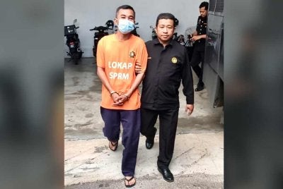 Suspek (kiri) dikawal anggota SPRM ketika keluar dari lokap mahkamah selepas selesai mengambil perintah reman. Foto: SPRM