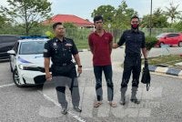 Tertuduh (tengah) dikawal polis ketika berjalan menuju ke lokap Mahkamah Kota Bharu. 