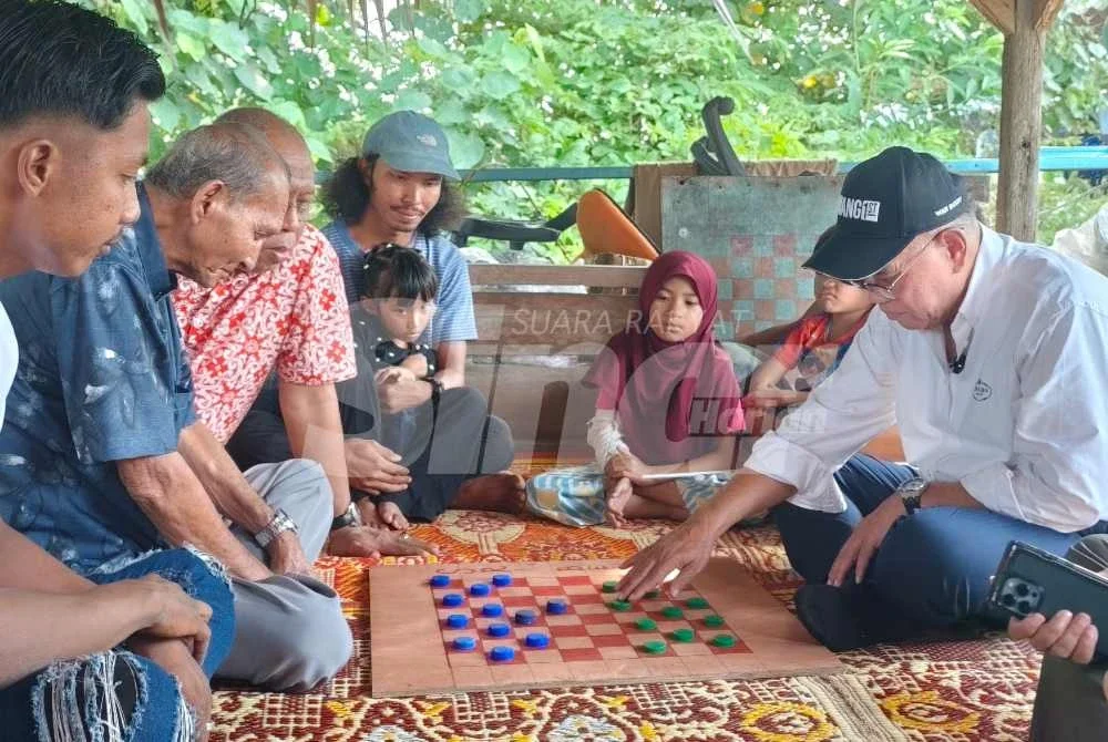 Wan Rosdy meluangkan masa bermain dam dengan salah seorang penduduk dalam program Jelajah Aspirasi Pahang 1st DUN Inderapura di Jeti Nelayan Sungai Belat, Kampung Belukar pada petang Rabu.