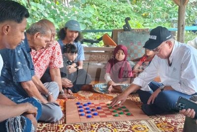 Wan Rosdy meluangkan masa bermain dam dengan salah seorang penduduk dalam program Jelajah Aspirasi Pahang 1st DUN Inderapura di Jeti Nelayan Sungai Belat, Kampung Belukar pada petang Rabu.
