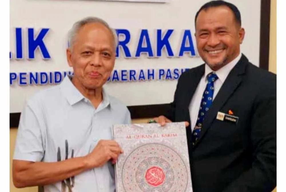 Muhammad Nasir (kiri) menyampaikan naskah al-Quran baharu kepada Samsudin pada Program Pemurnian Al-Quran Lusuh Sekolah-Sekolah Menengah Peringkat PPD Pasir Puteh 2026 yang diadakan di Dewan Seminar, PPD Pasir Puteh pada Ahad.