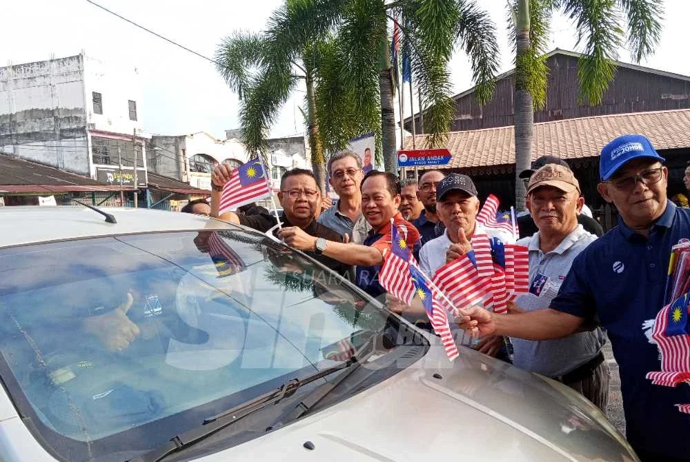 Ahmad (tengah) bersama sukarelawan menyerahkan Jalur Gemilang kepada penduduk di Pasar Pagi Benut pada Sabtu.
