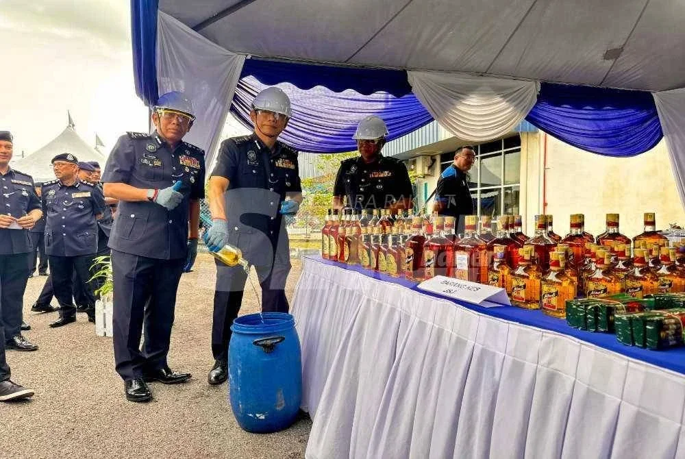 Dennis (tengah) melupuskan arak yang dirampas.