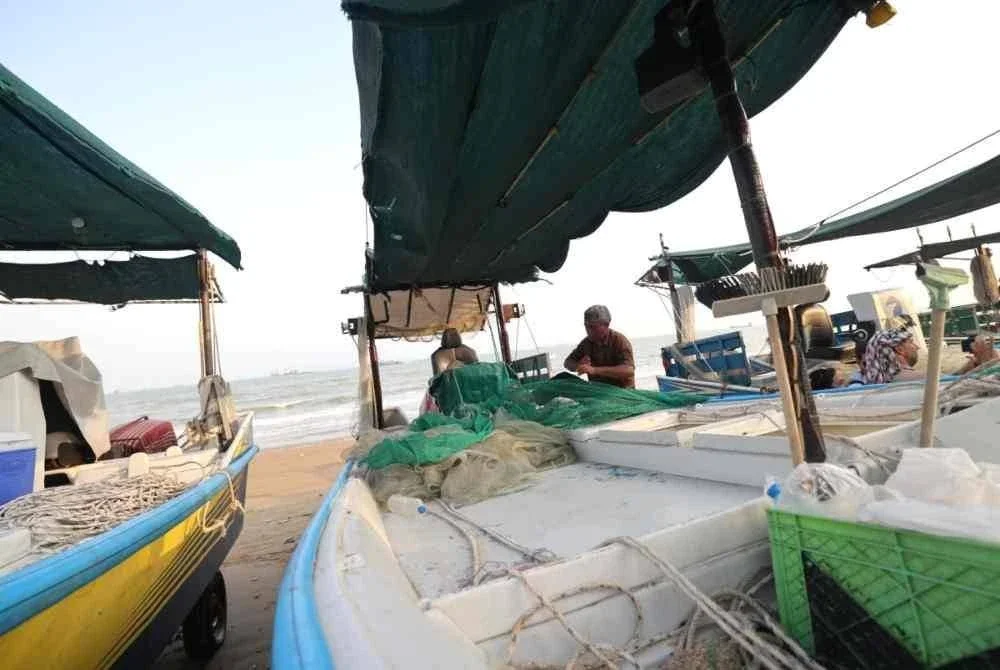 Nelayan membaiki pukat yang koyak di atas bot yang ditempatkan di tepi pantai Bandar Abbas.