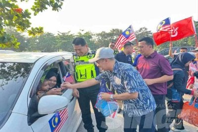 Mohd A Aruwan (tengah) dan Ismail (kiri) yang menyerahkan bendera kepada penggguna jalan raya. FOTO: ADILA SHARINNI WAHID