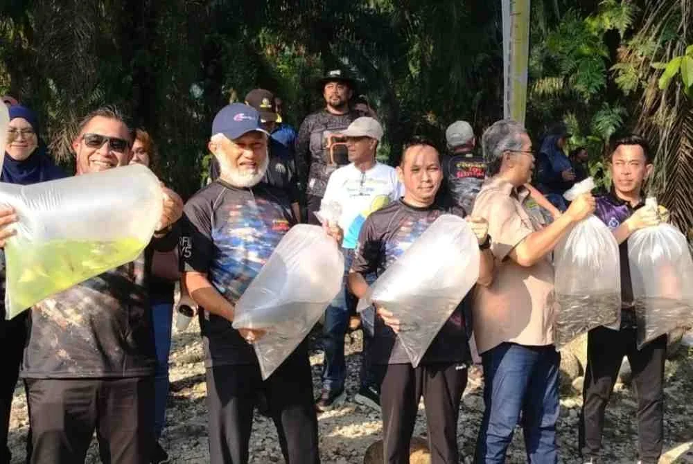 Mohd Ghazali (dua dari kiri) bersama Mohd Azlan (tengah) sebelum melepaskan ikan selepas menghadiri program Randuk for Lampam Volume 5 di Sahom Valley Resort, di sini pada Sabtu.