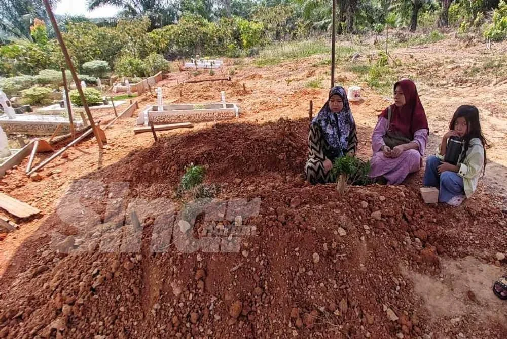Siti Aisyah (tengah) berada di pusara adiknya, arwah Muhamad Muazam Shah Kamardin meninggal dunia selepas dipatuk tedung selar ketika menjalani latihan demonstrasi pengendalian reptilia.