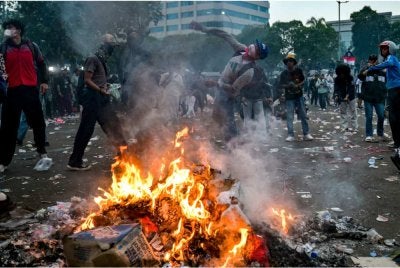 Seorang penunjuk perasaan membaling objek berhampiran timbunan poster dan sepanduk yang dibakar ketika demonstrasi di luar bangunan Parlimen di Jakarta. Foto: AFP