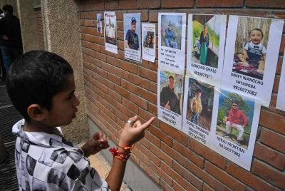 Seorang kanak-kanak melihat gambar individu yang masih hilang susulan banjir kilat di sebuah hospital di Kathmandu pada 28 Ogos lalu. - AFP