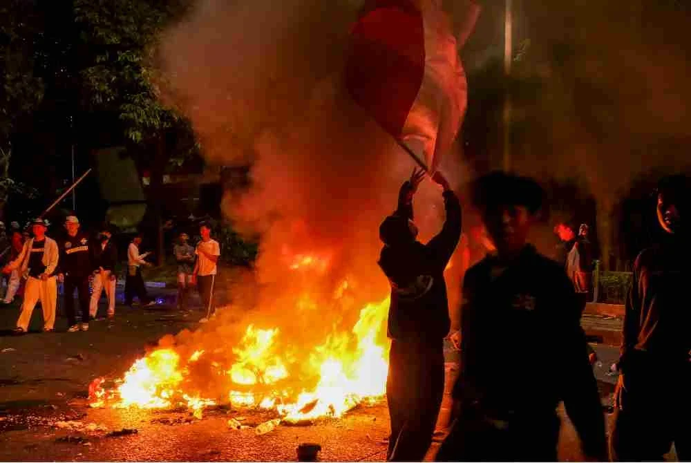 Penunjuk perasaan melintasi motosikal polis yang terbakar ketika seorang lelaki mengibarkan bendera Indonesia dalam demonstrasi tersebut. Foto: AFP