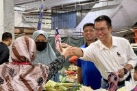 Hong Pin (kanan) mengedarkan Jalur Gemilang kepada orang ramai di Bakri, Muar.