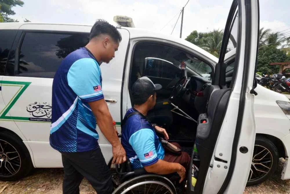 Md Shahrul Nizam (kanan) terpaksa dibantu untuk masuk ke dalam van jenazah yang dipandunya kerana lumpuh paras pinggang yang dialaminya sejak 2016 akibat kemalangan di tempat kerja ketika ditemui Bernama di Kampung Gaung. Foto Bernama