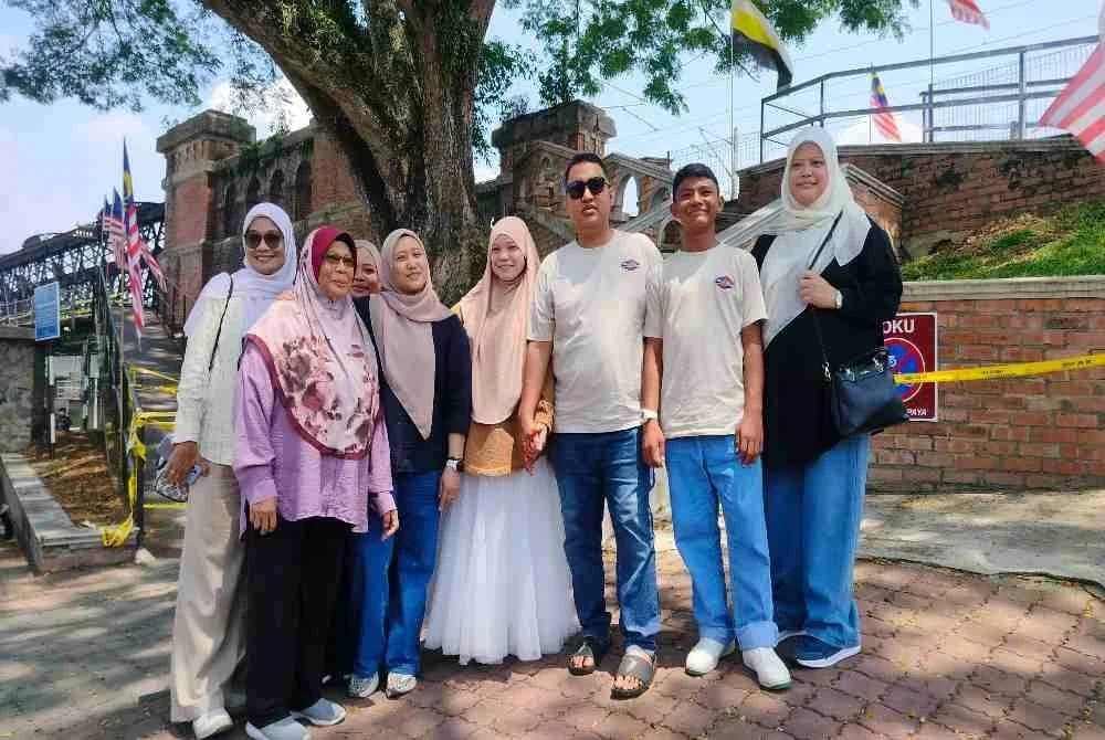 Siti Hazar (empat dari kiri) bersama keluarga dari Melaka sedikit kecewa hanya dapat bergambar di bahagian bawah Jambatan Victoria susulan penutupan pusat tumpuan pelancong tersebut.