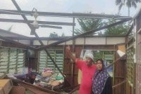 Zainuddin dan Roslinda menunjukkan bahagian atas kediaman pusaka yang rosak teruk akibat ribut dipercayai berpunca daripada fenomena belalai gajah pada Rabu.