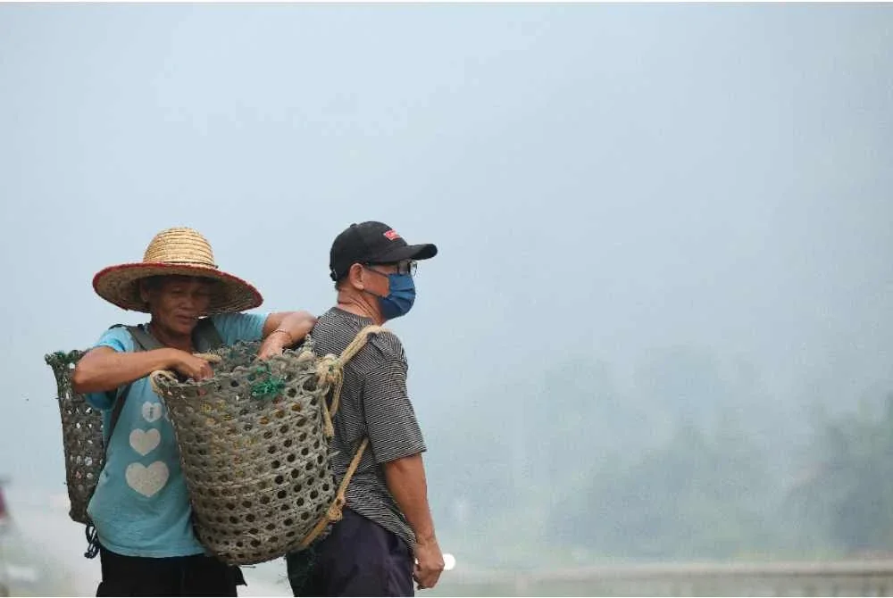 Dua penduduk Kampung Rasau, Serian, Rikat Tanggok (kanan) dan isterinya, Jumi Buu (kiri), sibuk menjual durian di tepi Jalan Serian-Sri Aman dalam suasana jerebu pada Jumaat. Foto Bernama