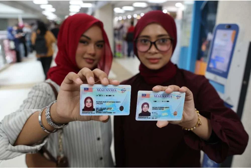 Puteri Nur Syafiqah Jailani (kiri) bersama Intan Syerina Ahmad Nizam menunjukkan kad pengenalan baharu. Foto Bernama