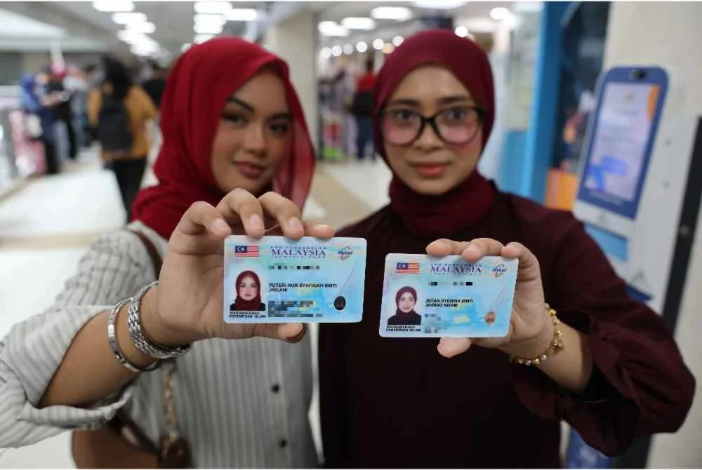 Puteri Nur Syafiqah Jailani (kiri) bersama Intan Syerina Ahmad Nizam menunjukkan kad pengenalan baharu pada hari pertama pengeluaran MyKad Generasi Baharu di Jabatan Pendaftaran Negara pada Khamis. Foto Bernama