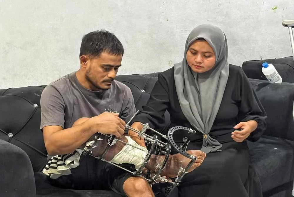 Nurma Lissa (kanan) membantu suaminya, Kamal Ridzuan melaraskan besi sokongan pada kaki kanannya yang mengalami kecederaan parah.