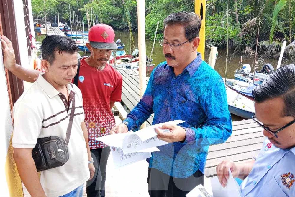 Md Israk (dua dari kanan) menunjukkan laporan analisis sample air sungai kepada nelayan di Jeti Kampung Simpang Kiri.