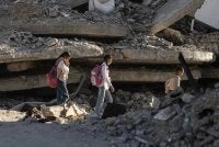 Kanak-kanak Palestin berjalan ke sekolah di celah runtuhan bangunan yang musnah ketika sesi akademik bermula di Khan Yunis, selatan Gaza. - AFP