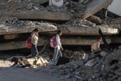 Kanak-kanak Palestin berjalan ke sekolah di celah runtuhan bangunan yang musnah ketika sesi akademik bermula di Khan Yunis, selatan Gaza. - AFP
