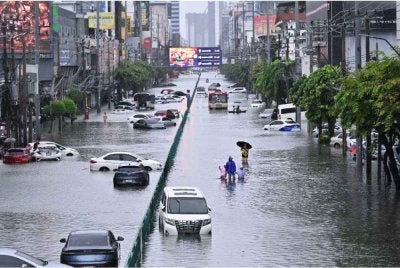 Orang ramai berjalan melepasi kenderaan yang ditinggalkan di Jalan Phetchaburi yang dilanda banjir. - Foto: AFP