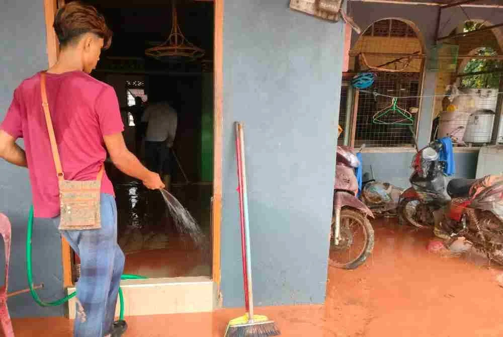 Penduduk membersihkan rumah yang terjejas banjir lumpur.