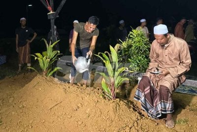 Mohamad Sanuzi (tengah) menyirami pusara anak dan bekas isterinya di di Tanah Perkuburan Dusun, Telaga Bata, Kota Bharu pada Isnin.