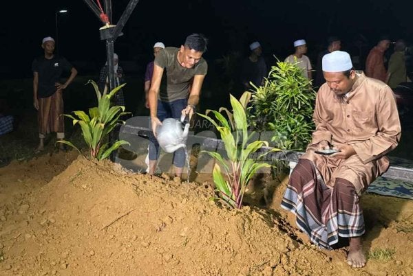 Mohamad Sanuzi (tengah) menyirami pusara anak dan bekas isterinya di di Tanah Perkuburan Dusun, Telaga Bata, Kota Bharu pada Isnin.