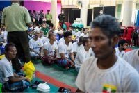 Migran Myanmar yang dihantar pulang dari Malaysia duduk sementara ketika proses sambutan rasmi ketibaan mereka di Thanlyin berlangsung. Foto: AFP
