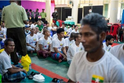 Migran Myanmar yang dihantar pulang dari Malaysia duduk sementara ketika proses sambutan rasmi ketibaan mereka di Thanlyin berlangsung. Foto: AFP