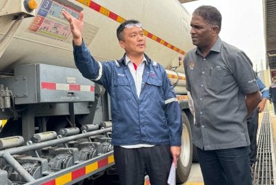 Michael (kiri) menerangkan mengenai lori tangki petrol yang terdapat di Depoh Chevron kepada Jegan.