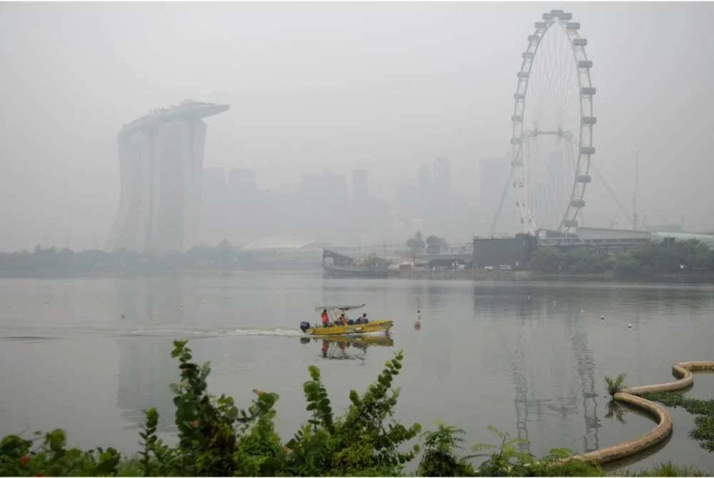 Sebuah bot melalui perairan berhampiran Marina Bay Sands ketika latar langit bandar Singapura diselubungi jerebu pada 15 Oktober 2026 susulan kebakaran hutan di Indonesia yang menjejaskan beberapa kawasan di rantau ini. - Foto AFP