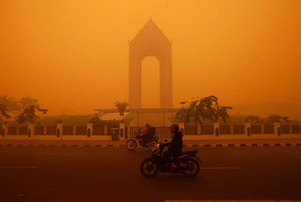 Penunggang motosikal melalui jalan raya pada waktu pagi di Palangkaraya, Kalimantan Tengah pada 14 Oktober 2026, dalam keadaan berjerebu tebal akibat kebakaran hutan dan tanah di kawasan berkenaan. Foto AFP