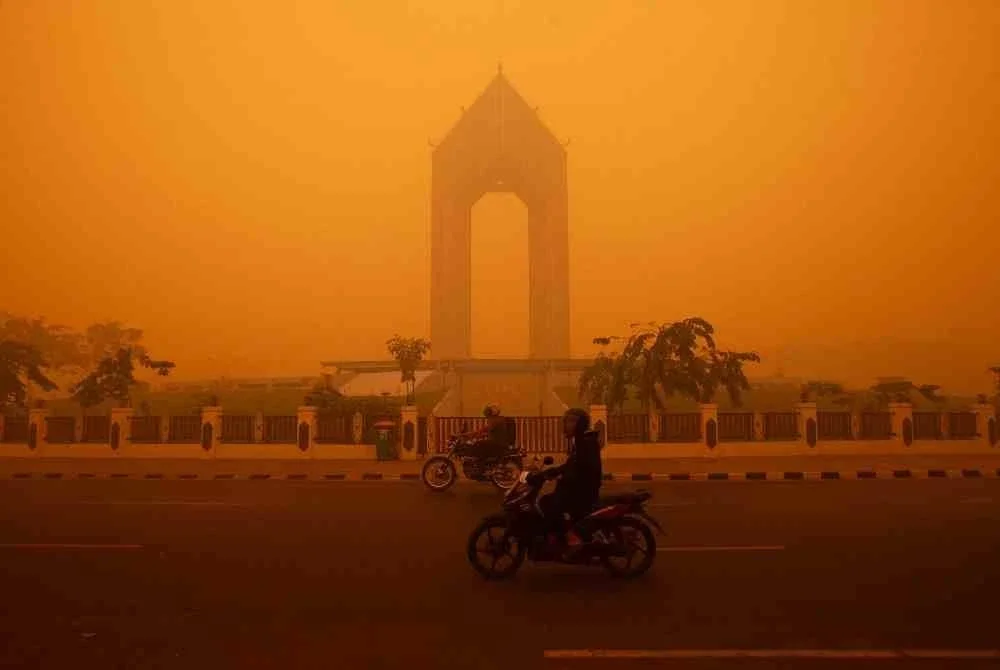 Penunggang motosikal meneruskan perjalanan pada waktu pagi dalam keadaan jerebu tebal di Palangka Raya. Foto AFP