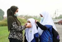 Seorang ibu memakaikan pelitup muka kepada anak-anaknya selepas pihak sekolah meminta murid memakai pelitup muka berikutan keadaan jerebu yang mencatatkan bacaan tidak sihat. Foto Bernama