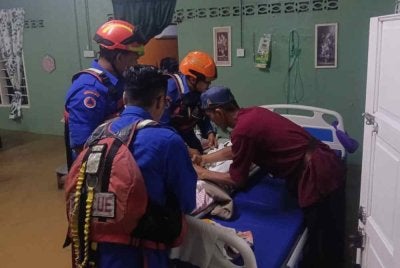 Anggota APM membantu memindahkan seorang pesakit lumpuh yang terperangkap dalam kejadian banjir kilat di dua buah kampung di Changlun pada malam Sabtu.