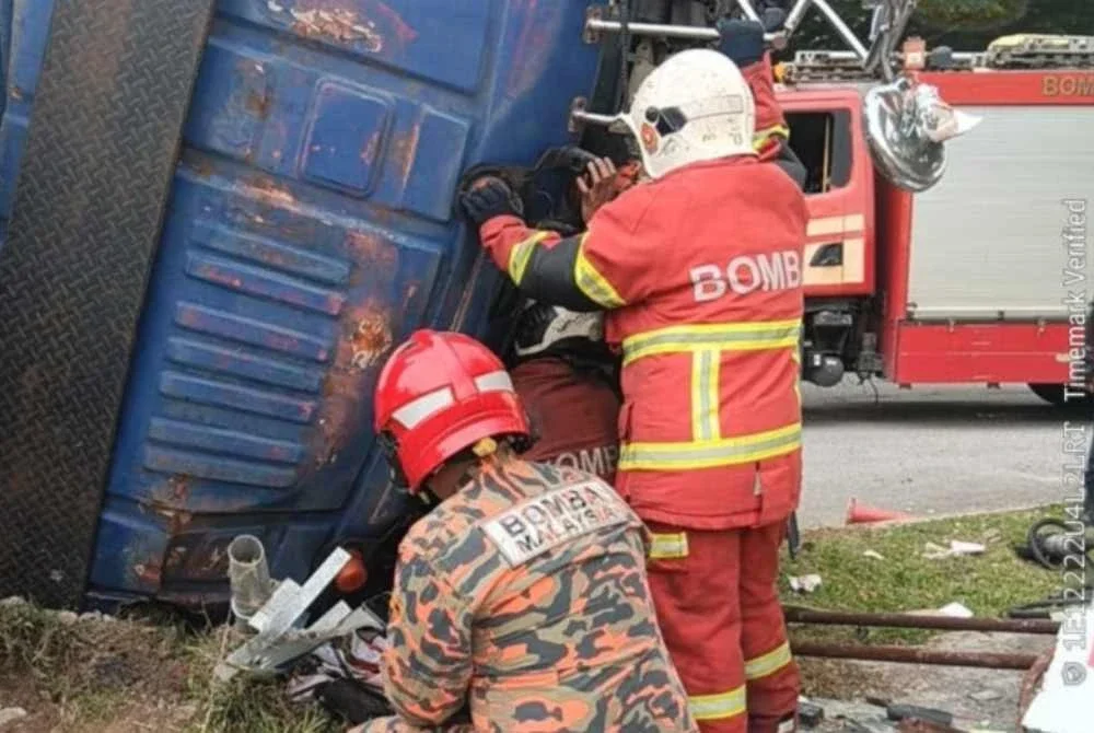 Anggota bomba berusaha mengeluarkan mangsa yang tersepit bahagian hadapan lori. - FOTO: JBPM Selangor