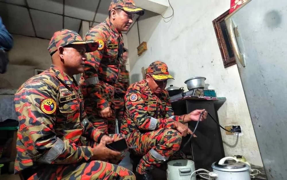 Nor Arifin(kanan) memeriksa penyambungan elektrik yang dilakukan di sebuah asrama pekerja warga asing 