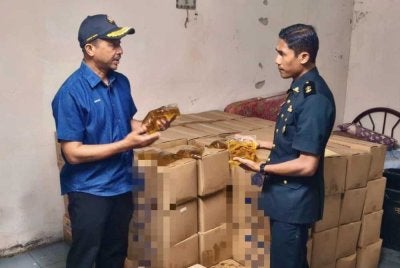 Muhammad Nizam (kiri) memeriksa minyak masak peket bersubsidi yang ditemui di gudang pakaian tersebut.
