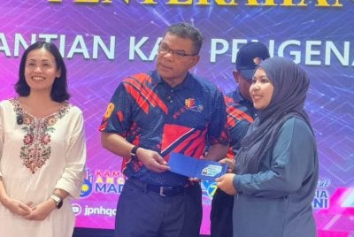 Saifuddin (tengah) menyerahkan Mykad generasi baharu di Dewan Serbaguna Kampung Melayu Sedenak, Kulai.