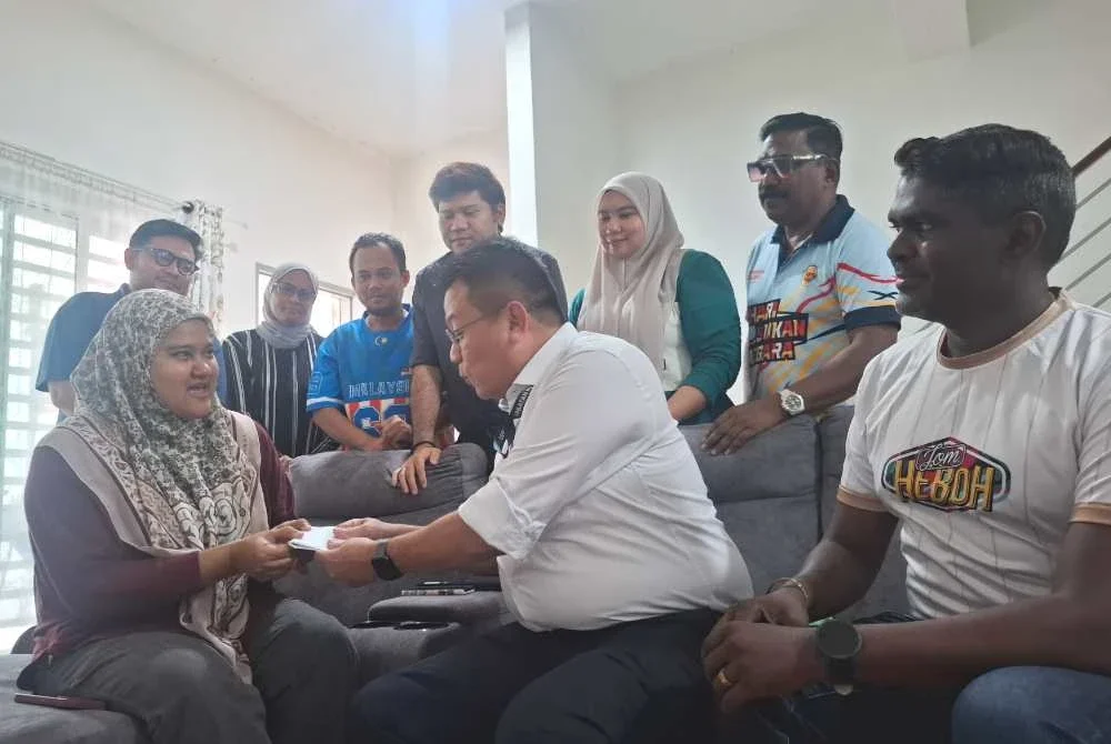 Shuhaimi (duduk, tengah) menyampaikan sumbangan Ahmad Zahid kepada Zahratulhayat di Medan Klebang Harmoni 2, Chemor pada Isnin.