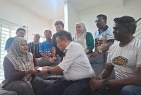 Shuhaimi (duduk, tengah) menyampaikan sumbangan Ahmad Zahid kepada Zahratulhayat di Medan Klebang Harmoni 2, Chemor pada Isnin.