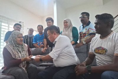 Shuhaimi (duduk, tengah) menyampaikan sumbangan Ahmad Zahid kepada Zahratulhayat di Medan Klebang Harmoni 2, Chemor pada Isnin.