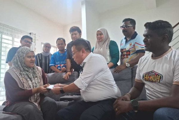 Shuhaimi (duduk, tengah) menyampaikan sumbangan Ahmad Zahid kepada Zahratulhayat di Medan Klebang Harmoni 2, Chemor pada Isnin.